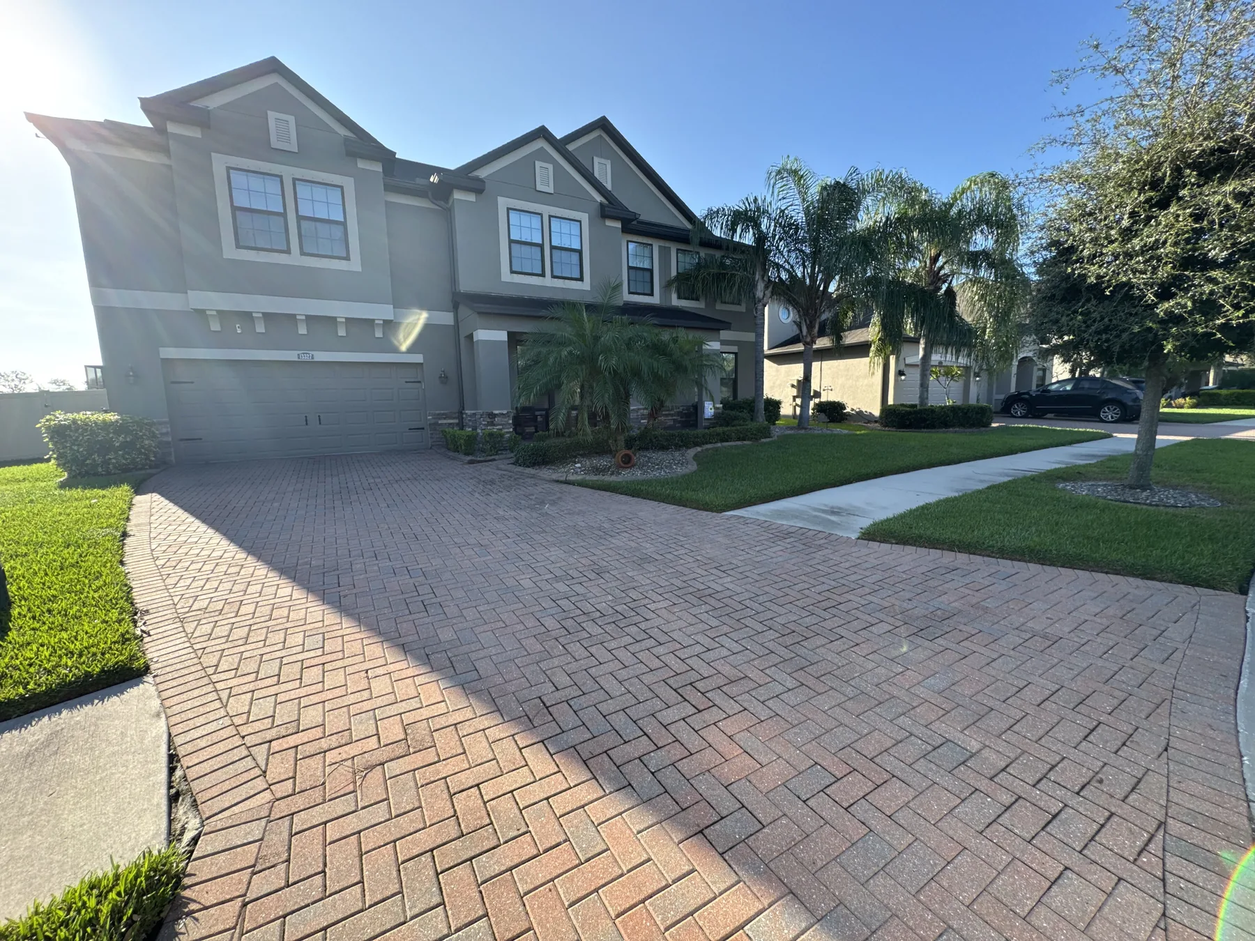 Large paver driveway framed by maintained lawn and palms